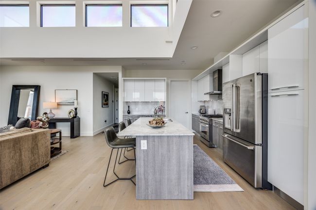 Kitchen featuring premium appliances, white cabinetry, modern cabinets, wall chimney range hood, and a breakfast bar | Image 13
