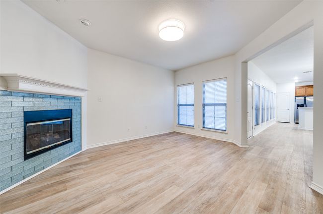 This warm and welcoming living room is the heart of the home, featuring a cozy fireplace that adds charm and comfort year-round. Light-colored flooring enhances the sense of openness and reflects the natural light streaming through large windows, creating a bright and airy atmosphere. | Image 7