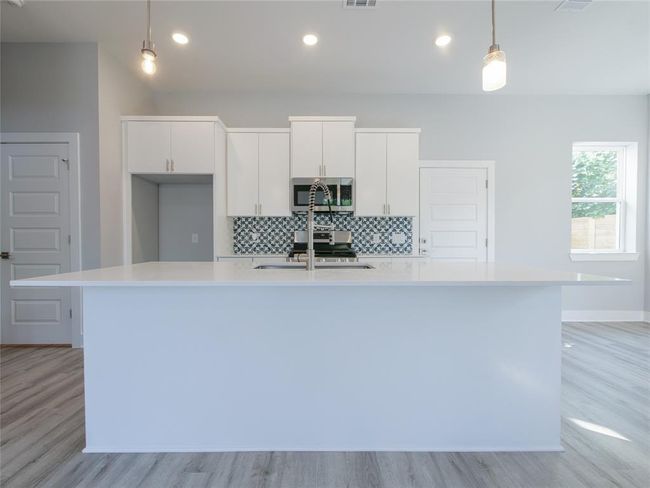 Kitchen featuring stainless steel microwave, light wood-style flooring, a large island with sink, light countertops, and white cabinetry | Image 9