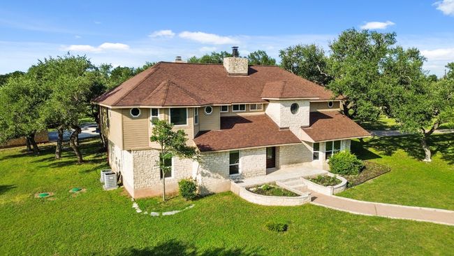 View of front facade featuring stone siding, a chimney, roof with shingles, a front lawn, and a patio area | Image 38