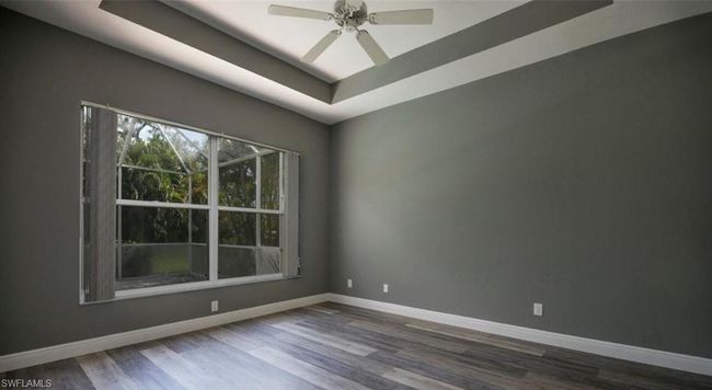 Empty room featuring a raised ceiling, dark hardwood / wood-style floors, and ceiling fan | Image 9