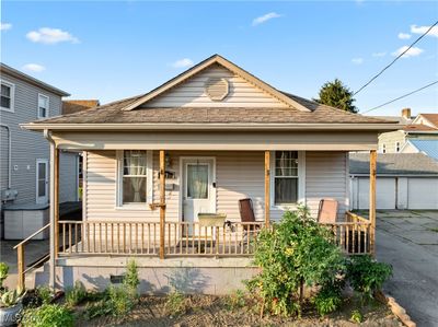 Bungalow-style house with a porch, a garage, and an outdoor structure | Image 1