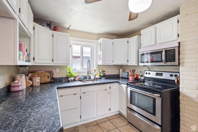 Kitchen featuring dark stone countertops, a sink, light tile patterned floors, stainless steel appliances, and white cabinets | Image 7