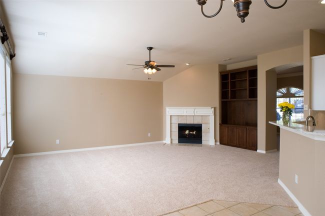 Unfurnished living room featuring light colored carpet, arched walkways, a fireplace, a ceiling fan, and lofted ceiling | Image 8
