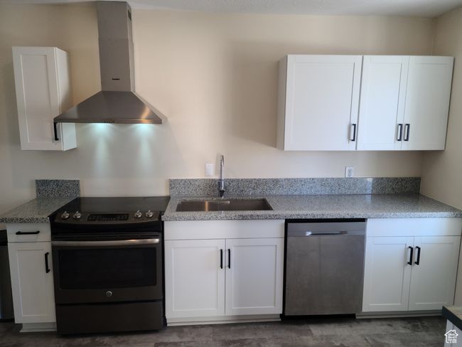 Kitchen featuring stainless steel appliances, wall chimney exhaust hood, a sink, and white cabinets | Image 8