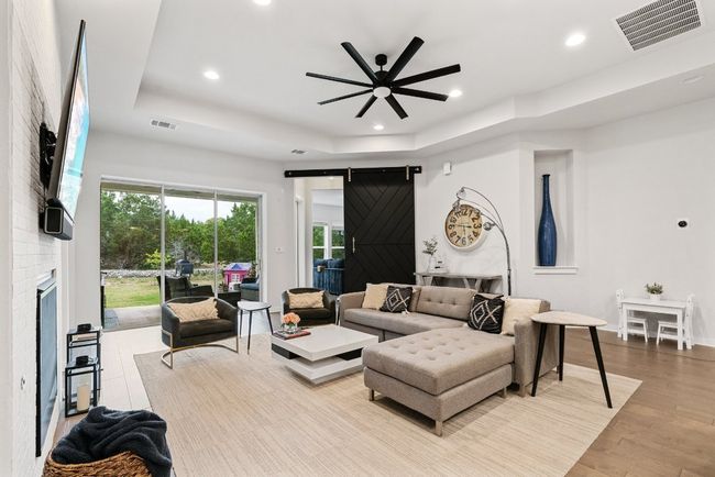 Living area with a raised ceiling, ceiling fan, recessed lighting, a fireplace, and a barn door | Image 14
