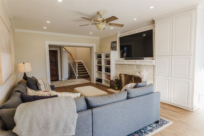 Living room featuring light wood-type flooring, ceiling fan, ornamental molding, and a stone fireplace | Image 12