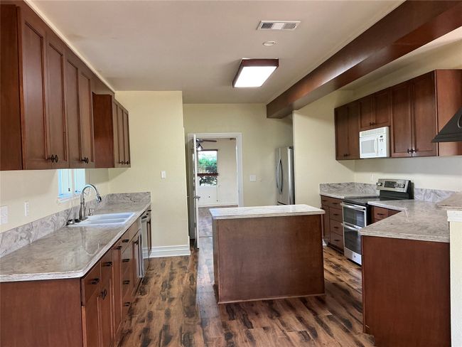 Kitchen featuring a sink, dark wood finished floors, appliances with stainless steel finishes, visible vents, and a kitchen island | Image 6