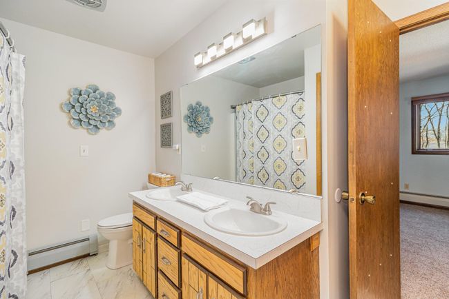 The full bathroom features a dual sink vanity with storage, an exhaust fan, vinyl tile and access to both bedrooms. | Image 25
