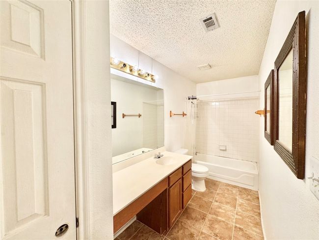 Full bath featuring vanity, a textured ceiling, shower / bath combination with curtain, and tile patterned flooring | Image 12