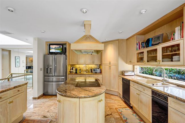 Kitchen featuring light stone counters, a sink, light brown cabinets, a kitchen island, and black appliances | Image 9