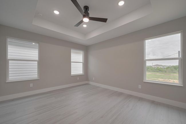 Airy and expansive, the primary bedroom showcases multiple large windows, a tray ceiling with recessed lighting, and a modern ceiling fan for added comfort. | Image 20