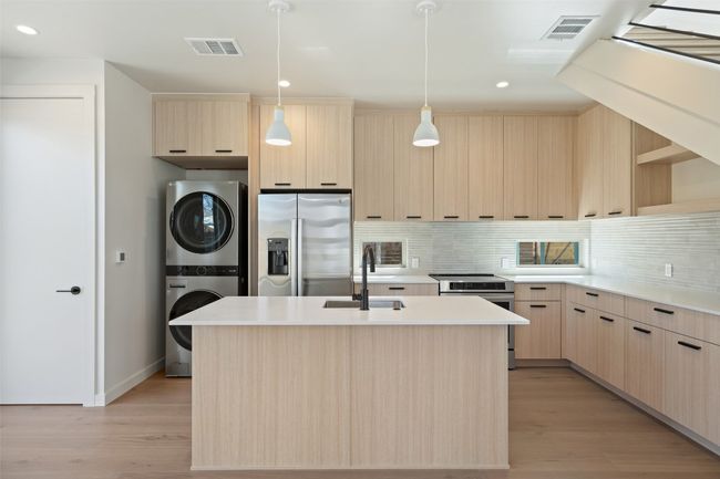 Kitchen with appliances with stainless steel finishes, stacked washer / drying machine, visible vents, and light brown cabinetry | Image 24