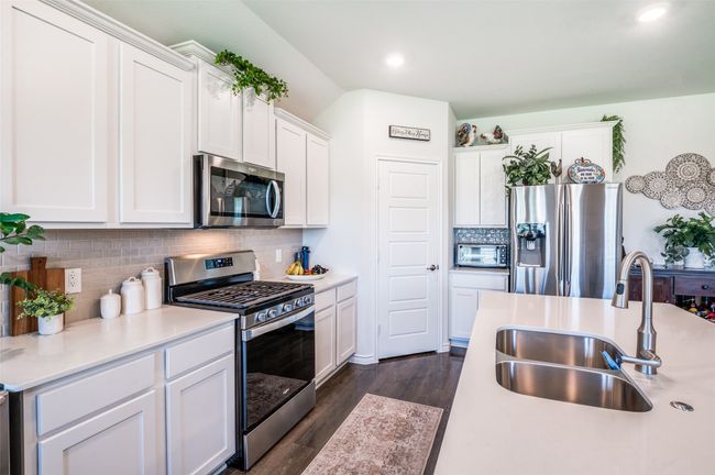Kitchen with stainless steel appliances, light countertops, white cabinetry, backsplash, and dark wood finished floors | Image 13