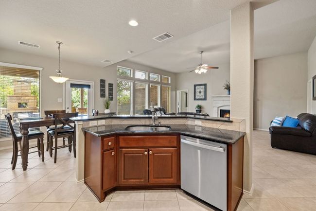 Kitchen with stainless steel dishwasher, open floor plan, ceiling fan, light tile patterned floors, and hanging light fixtures | Image 9