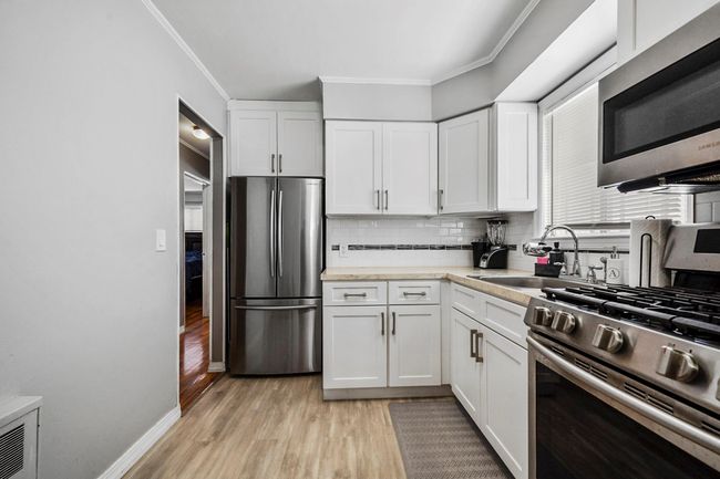 Kitchen featuring stainless steel appliances, backsplash, a sink, crown molding, and light wood-style flooring | Image 6