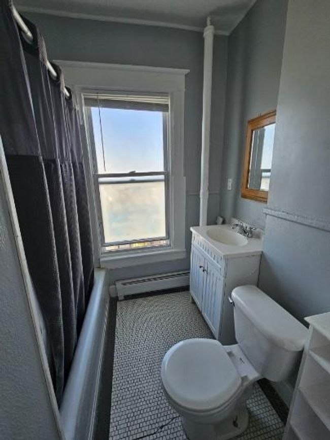 Full bath featuring a baseboard heating unit, vanity, toilet, and plenty of natural light | Image 7