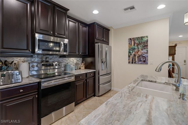 Kitchen with backsplash, a sink, light stone countertops, stainless steel appliances, and visible vents | Image 7