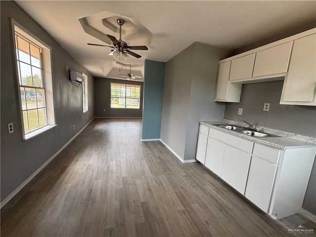 Kitchen with a sink, a wall mounted AC, dark wood finished floors, a ceiling fan, and baseboards | Image 4