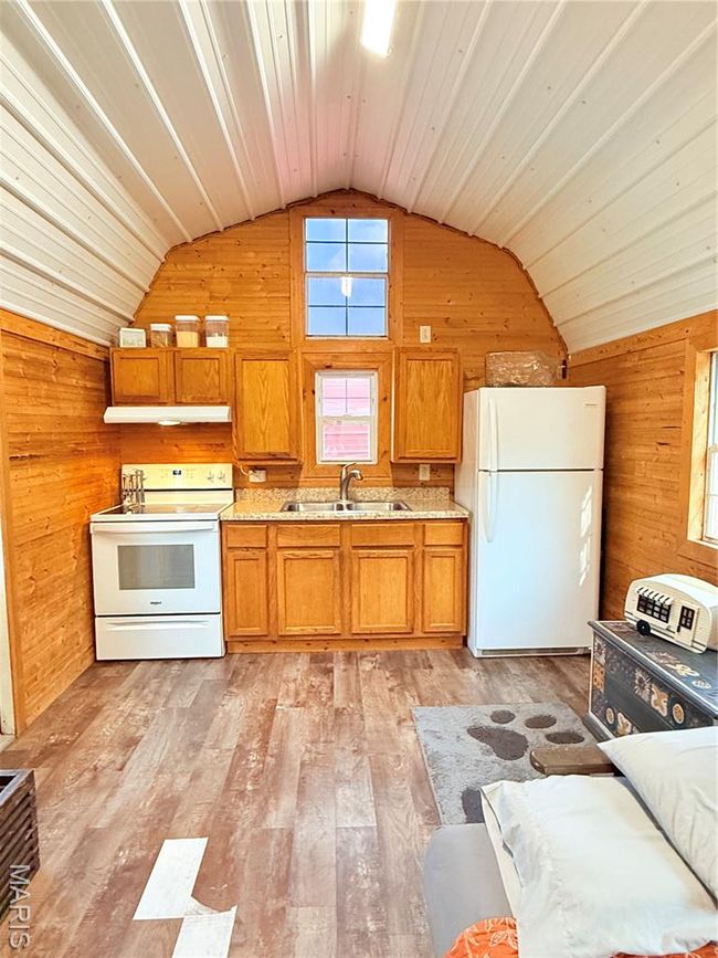 Kitchen with fridge, stove, a sink, lofted ceiling, and wood walls | Image 11