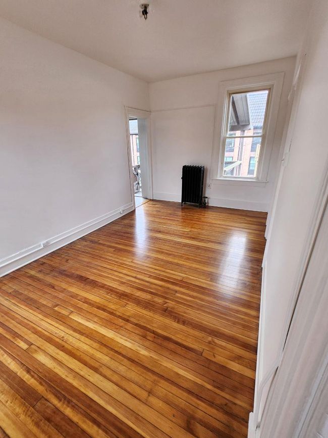 Unfurnished living room featuring radiator, plenty of natural light, wood finished floors, and baseboards | Image 8
