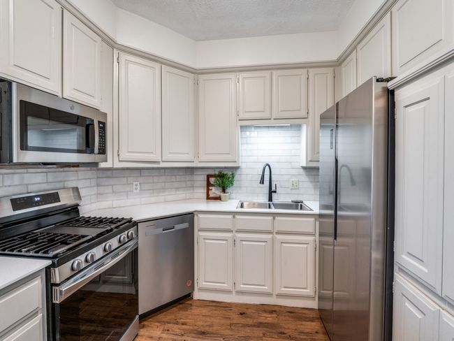 Kitchen featuring stainless steel appliances, light countertops, dark wood-style floors, backsplash, and a textured ceiling | Image 11