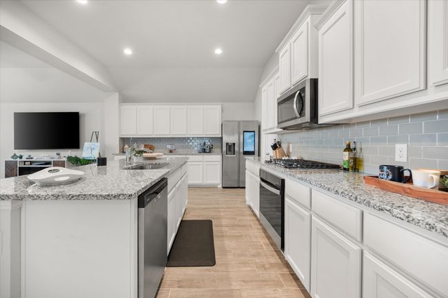 Kitchen featuring appliances with stainless steel finishes, white cabinetry, light wood-type flooring, a kitchen island with sink, and recessed lighting | Image 6