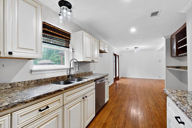 Kitchen with dishwasher, ornamental molding, wood finished floors, dark stone countertops, and white cabinets | Image 10