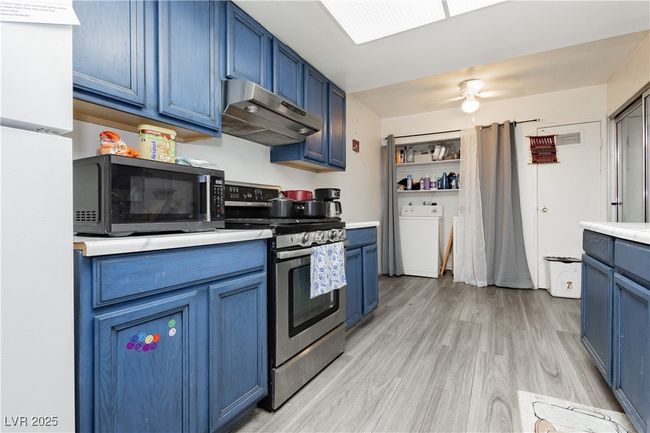 Kitchen featuring black microwave, washer / clothes dryer, stainless steel range oven, blue cabinetry, and under cabinet range hood | Image 9