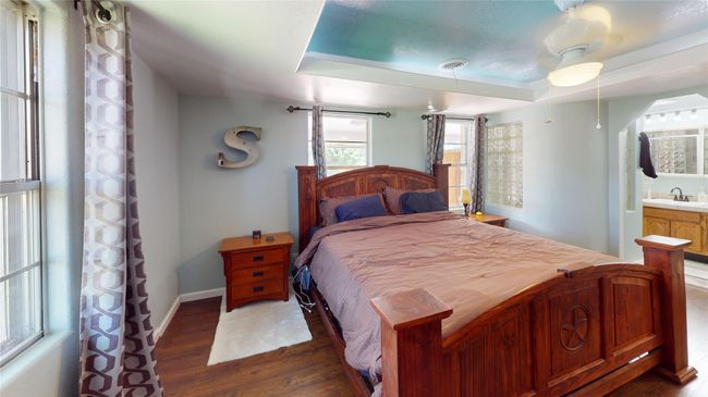 Bedroom with dark wood-style floors, a raised ceiling, and connected bathroom | Image 23