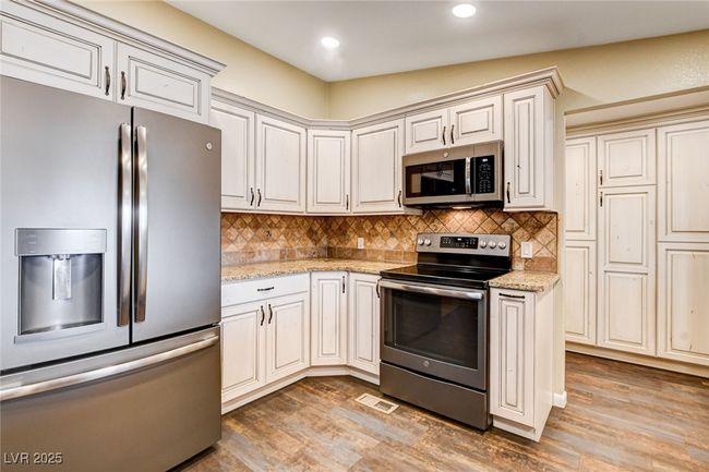 Kitchen featuring stainless steel appliances, light wood-type flooring, tasteful backsplash, light stone counters, and recessed lighting | Image 24