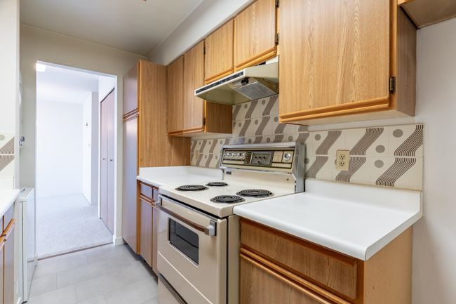 Kitchen with decorative backsplash, light countertops, under cabinet range hood, electric stove, and light tile patterned floors | Image 14