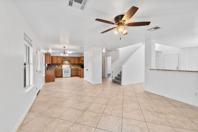 Unfurnished living room featuring light tile patterned flooring, a chandelier, stairs, ceiling fan, and baseboards | Image 11