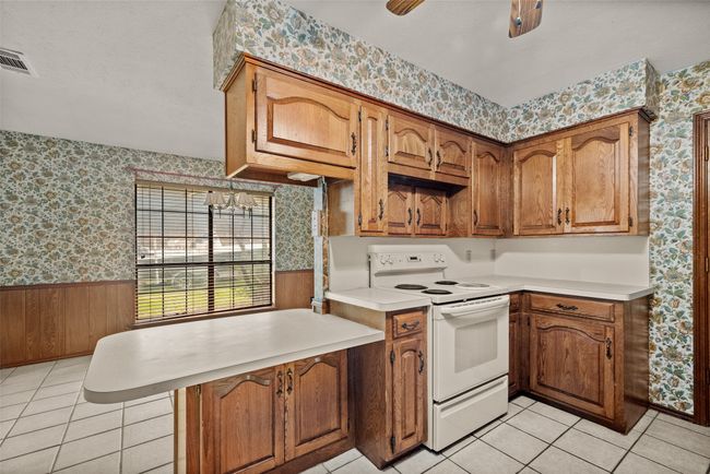 Kitchen featuring light countertops, a peninsula, wallpapered walls, white range with electric stovetop, and wainscoting | Image 12