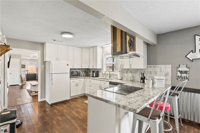 Kitchen featuring freestanding refrigerator, a peninsula, stainless steel microwave, white cabinets, and light stone counters | Image 11