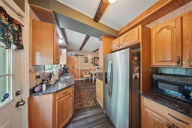 Kitchen with stainless steel fridge with ice dispenser, dark wood-style flooring, black microwave, decorative backsplash, and dark stone countertops | Image 11