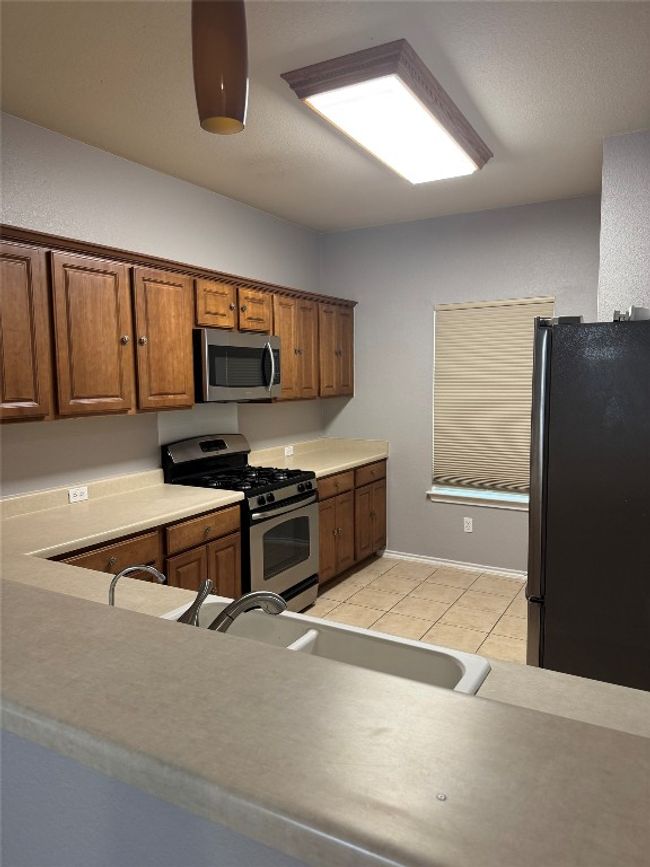 Kitchen featuring stainless steel appliances, light tile patterned floors, brown cabinets, light countertops, and a sink | Image 6