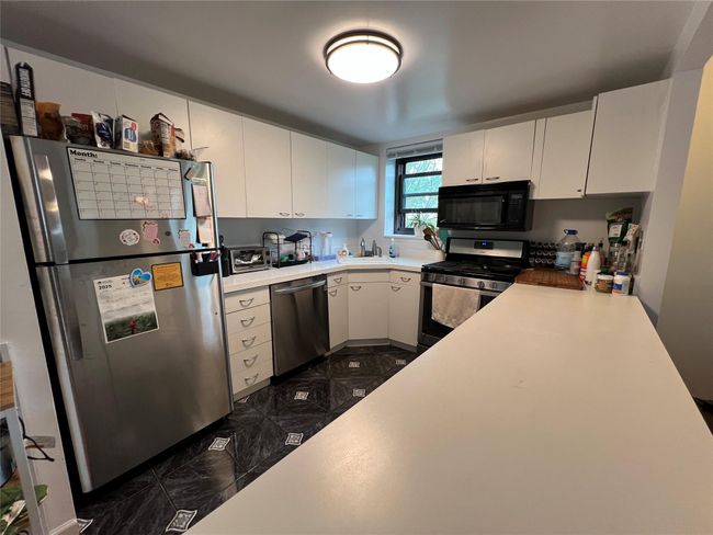 Kitchen with a sink, black microwave, dishwasher, light countertops, and freestanding refrigerator | Image 5