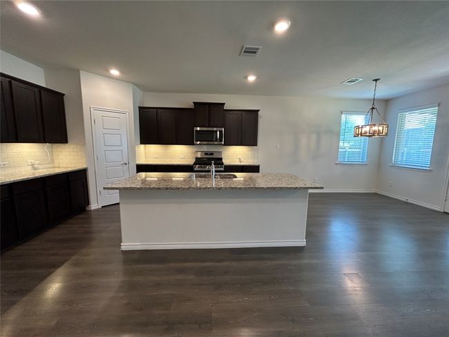 Kitchen featuring appliances with stainless steel finishes, light stone counters, dark wood finished floors, tasteful backsplash, and a kitchen island with sink | Image 6