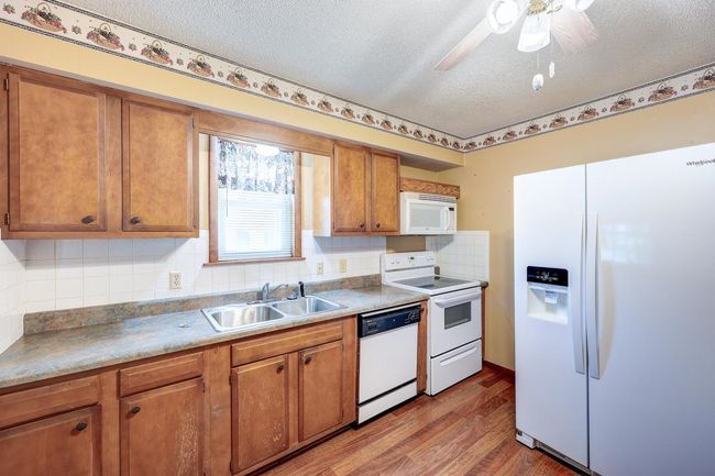 Kitchen featuring white appliances, a sink, a textured ceiling, light wood-style floors, and brown cabinetry | Image 7