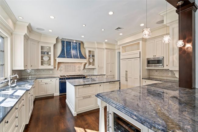 Kitchen with custom exhaust hood, sink, built in appliances, decorative light fixtures, and dark stone countertops | Image 7