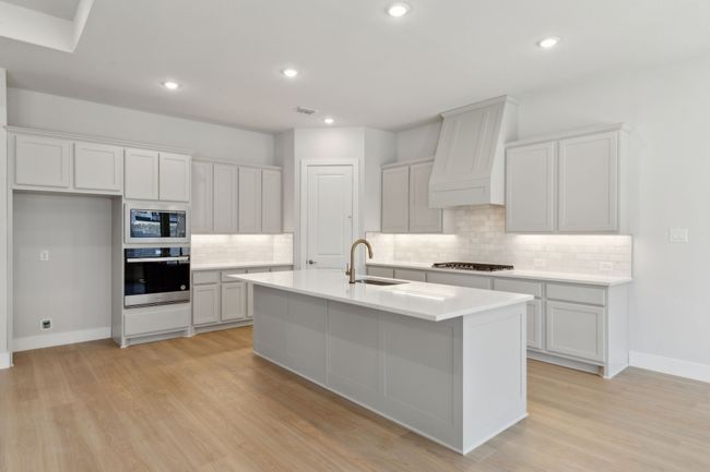 Kitchen featuring appliances with stainless steel finishes, decorative backsplash, a kitchen island with sink, light wood-style floors, and light countertops | Image 15