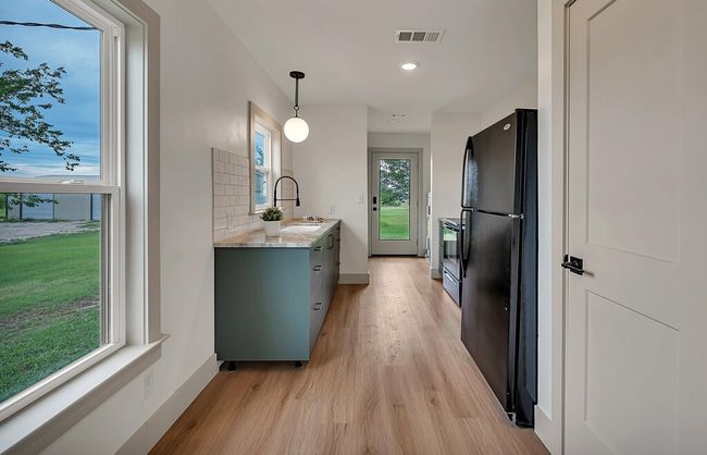 Guest House Kitchen with freestanding refrigerator, light wood-type flooring, light stone countertops, stainless steel range oven, and decorative light fixtures | Image 36