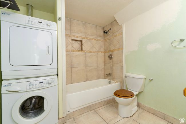 Full bath with stacked washer and clothes dryer, tile patterned flooring, baseboards, toilet, and bathing tub / shower combination | Image 31