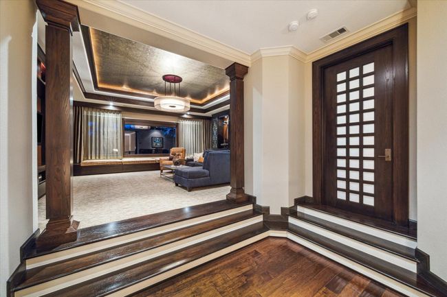 A circular staircase topped by a magnificent rotunda ceiling with exquisite lighting leads up to this dramatic split-level entry to the second-floor game room and home gym. Framed by richly stained wood columns and millwork, the rich tones are echoed in the game room’s tray ceiling, which features a gold leaf inset, cove lighting, and a contemporary chandelier that adds a touch of glam. The ambient light provided by the trio of windows and custom lighting creates an inviting atmosphere. | Image 35