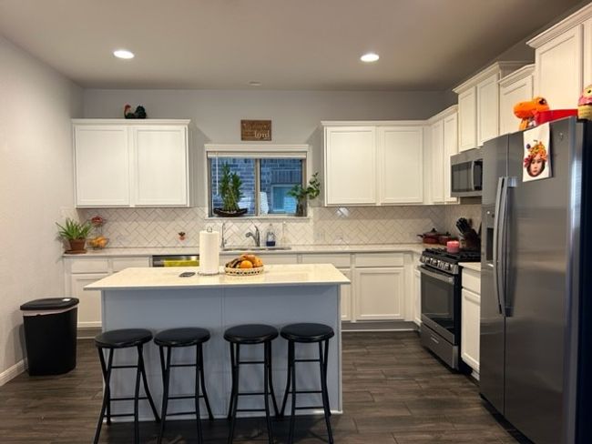 Kitchen with a sink, light countertops, stainless steel appliances, white cabinetry, and a kitchen bar | Image 13