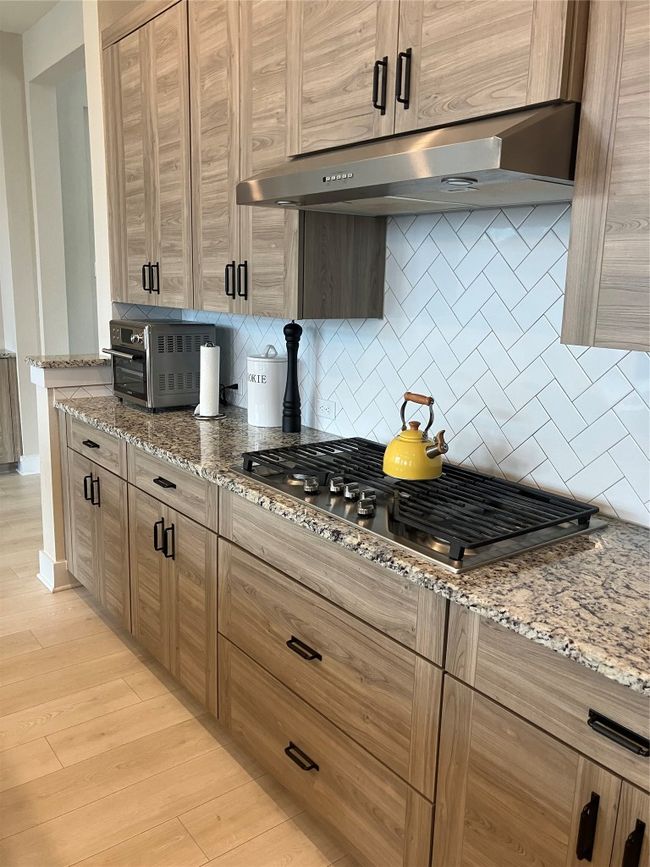 Kitchen featuring extractor fan, tasteful backsplash, light stone counters, stainless steel gas stovetop, and light wood-style floors | Image 8