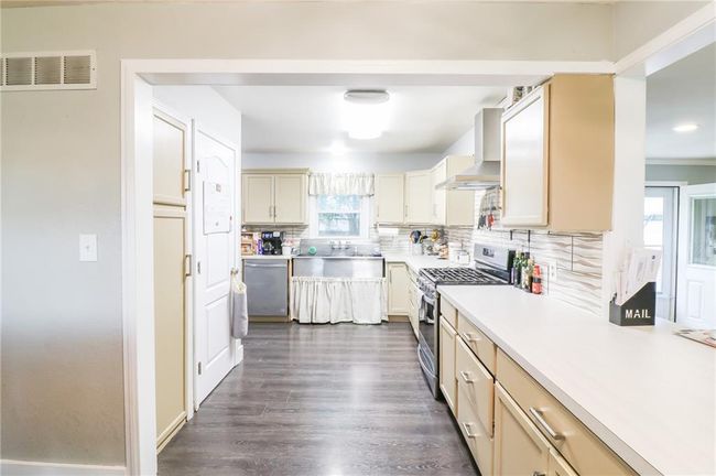 Kitchen with appliances with stainless steel finishes, wall chimney exhaust hood, backsplash, light countertops, and dark wood-type flooring | Image 13