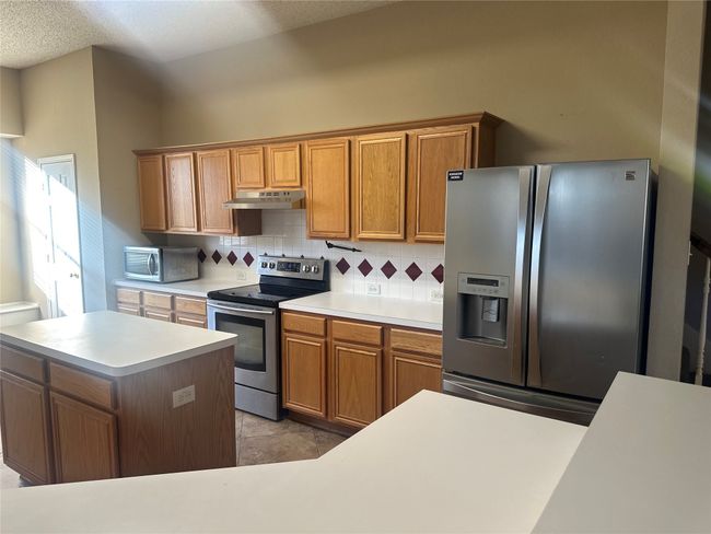 Kitchen featuring stainless steel appliances, under cabinet range hood, decorative backsplash, light countertops, and brown cabinets | Image 13