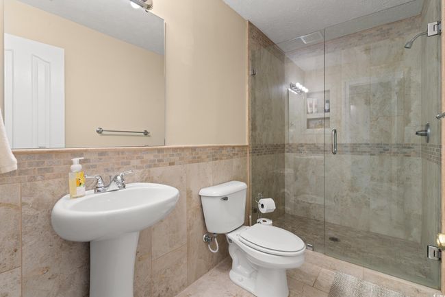 Bathroom featuring toilet, a stall shower, tile walls, a wainscoted wall, and tile patterned floors | Image 17